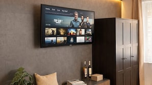 Ein modernes Wohnzimmer mit einem an der Wand befestigten Flachbildfernseher, einem Holzkonsolentisch mit Pflanze, Büchern und Flaschen sowie einem dunklen Holzschrank.