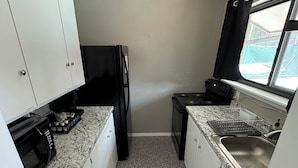 Une cuisine de taille réduite avec des meubles blancs, un réfrigérateur noir, une cuisinière et une fenêtre donnant sur un beau paysage.