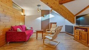 Ein gemütlicher Loftsraum mit einem roten Sofa, Holzboden und einem Fernseher auf einer Holzkommode.