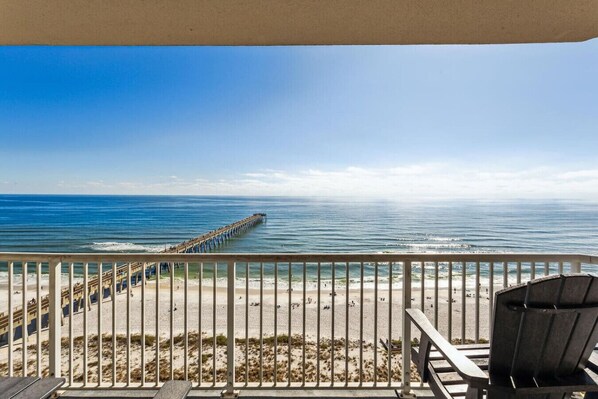 A balcony with a view of the ocean, a pier, and beach chairs. - Fiddler on The Reef, Navarre Beach FL (Navarre)