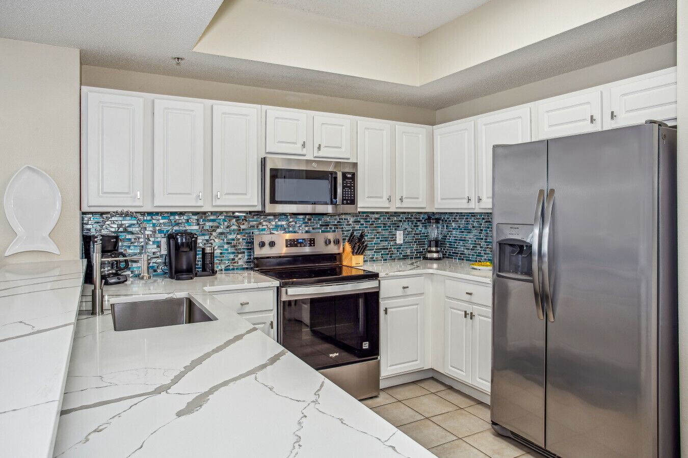 A modern kitchen with white cabinets, a stainless steel refrigerator, a microwave, and a built-in oven.