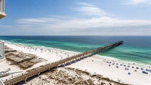 A beach with a long pier extending into the ocean, a sandy beach with umbrellas, and a clear sky. - Fiddler on The Reef, Navarre Beach FL (Navarre)