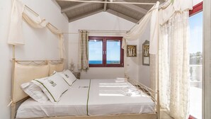 Ein Bett mit Baldachin, ausgestattet mit weißen Leinen und grünen Akzenten, ein Holzboden und ein Blick durch ein Fenster mit Vorhängen.