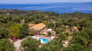 An aerial view of a coastal property with a swimming pool, surrounded by dense greenery and houses. - Amara Villa - Three Bedroom Villa, Sleeps 6 (Paxi)