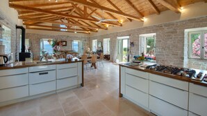 A spacious kitchen with a high ceiling and exposed beams, stone walls, and a large island with a gas stove. - Amara Villa - Three Bedroom Villa, Sleeps 6 (Paxi)