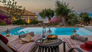 A poolside setting with lounge chairs, a table with a book, drinks, and a fruit bowl. - Amara Villa - Three Bedroom Villa, Sleeps 6 (Paxi)