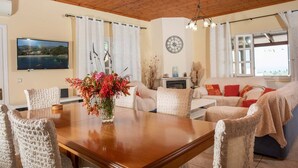 A cozy living room with a wooden dining table, comfortable seating, a fireplace, and a large window with a view.
