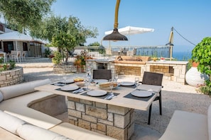 Un espacio de comedor al aire libre con mesas de piedra, asientos acolchados y vistas al mar.