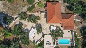 An aerial view of a property with a swimming pool, a covered outdoor seating area, and a red-roofed building.
