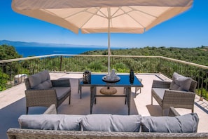 A balcony with wicker furniture, a table, and an umbrella.
