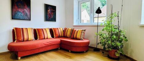 A modern living room with a red sectional sofa, two framed artworks, a large window, and a potted plant.