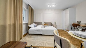 A modern, well-lit bedroom with a bed, bedside table, and a small dining area with a table and chairs.