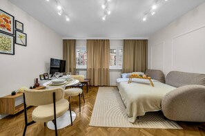 Ein modernes Hotelzimmer mit Bett, Sofa, Essbereich mit Tisch und Stühlen, Fernseher und einem fenster mit Vorhängen.