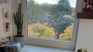 Une cuisine avec une grande fenêtre, un tabouret de bar, un réfrigérateur et une plante en pot.