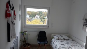 Une petite pièce, peu meublée, avec une fenêtre donnant sur un quartier résidentiel.