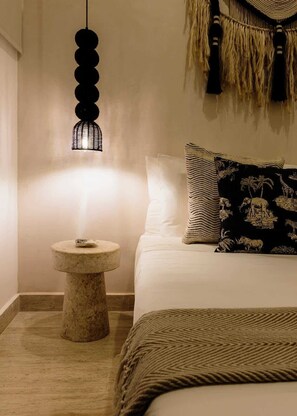A bedroom with a bed, a round side table, a hanging light fixture, and a wall hanging.