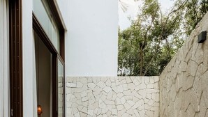 A wooden deck with a stone wall, a wooden chair, a round wooden stool, and a white planter.