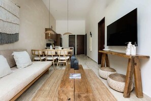 A modern living room with a sofa, dining table, chairs, and a TV. - Naiik Jungle Retreat Private Pool Beach Club (Tulum)