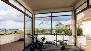 A modern gym with exercise equipment, large windows, and a view of palm trees.