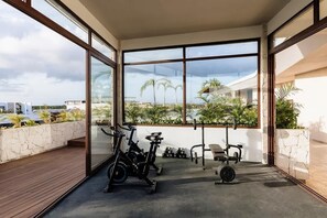 A modern gym with exercise equipment, large windows, and a view of palm trees. - Naiik Jungle Retreat Private Pool Beach Club (Tulum)