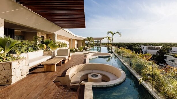 A modern outdoor pool area with a wooden deck, a curved seating area, and a view of the surrounding landscape.