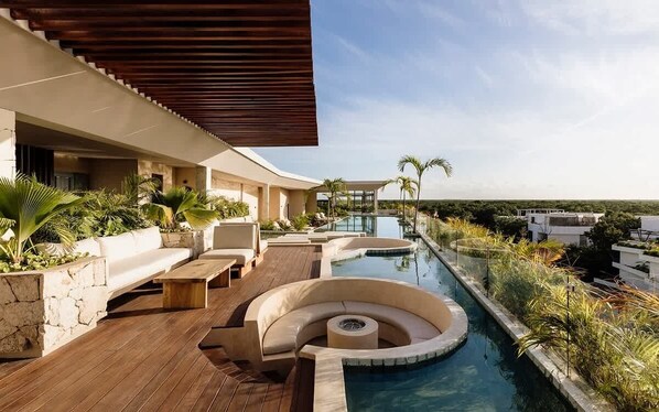 A modern outdoor pool area with a wooden deck, a curved seating area, and a view of the surrounding landscape.