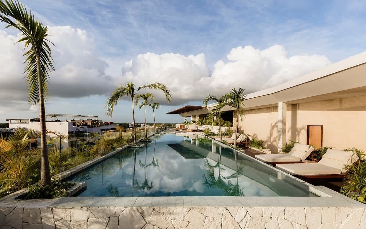 A swimming pool with lounge chairs, palm trees, and a modern building.