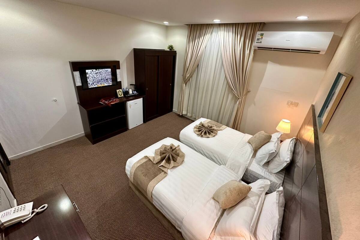Une chambre d’hôtel avec deux lits, un bureau avec un téléphone, une télévision, une armoire et un appareil de climatisation.