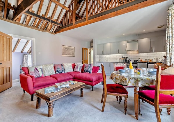 A spacious living room with a red sofa, wooden coffee table, and a dining area with a table and chairs.