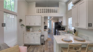 Una cocina moderna con armarios blancos, una isla central y una zona de comedor con sillas.