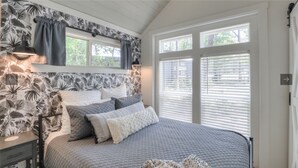 Un dormitorio con cama, mesita de noche, lámpara y ventana con persianas.