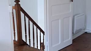 Una habitación con puerta blanca, escalera de madera y un radiador.