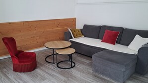 Un espacio de estar pequeño con un sofá gris, un sillón rojo y una mesa redonda de madera.