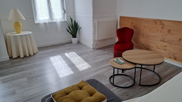 Una habitación moderna y luminosa con suelo de madera, una silla roja, una pequeña mesa redonda, una lámpara amarilla y una planta en maceta.