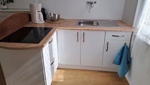 Cocina compacta con estufa negra, pileta de acero inoxidable y alacenas blancas.