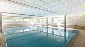 Una amplia piscina interior con ventanales transparentes, paredes y piso de azulejos.
