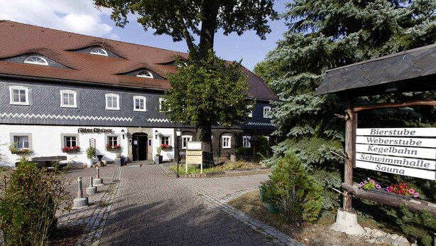 Un edificio tradicional con un patio adoquinado, un letrero que enumera Bierstube, Weberstube, Kegelebahn, Schwimmhalle y Sauna.