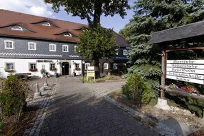 A traditional building with a cobblestone courtyard, a sign listing Bierstube, Weberstube, Kegelebahn, Schwimmhalle, and Sauna. - Landhotel Alter Weber  (Cunewalde)