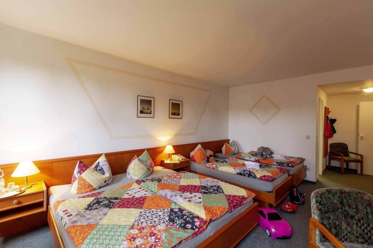 Habitación de hotel con dos camas, cada una con un edredón colorido, una mesita de noche con lámpara y una silla.