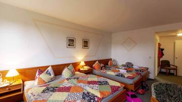 A hotel room with two beds, each with a colorful quilt, a nightstand with a lamp, and a chair.
