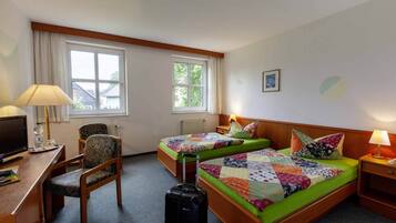 A hotel room with two single beds, a desk with a chair, a television, and a suitcase.