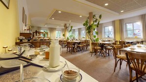 Un comedor amplio con varias mesas y sillas, un sistema de buffet y grandes ventanales que permiten la entrada de luz natural.