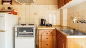 A compact kitchen with a white stove, a small oven, wooden cabinets, a sink, and a countertop with a kettle and a coffee maker. - Double Room Apartment (Poros kefalonias)
