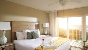 Ein Hotelzimmer mit einem großen Bett, einem Nachttisch, einer Lampe, einem Tablett mit Frühstücksgegenständen und einem Balkon mit Meerblick.