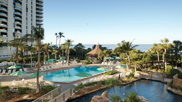 Ein Poolbereich eines Resorts mit mehreren Pools, Palmen und Blick auf den Ozean.