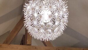 Un coin repas comprenant une table ronde, deux chaises, un élément décoratif central et un lustre original.