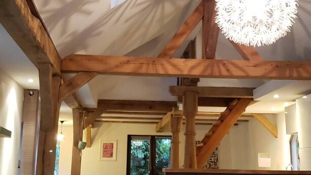 Un vaste hall doté de hauts plafonds, de poutres apparentes en bois, d’un lustre central et d’un escalier menant à un niveau supérieur.