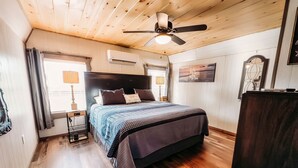 Un dormitorio con techo de madera, una cama con colcha a cuadros, un ventilador de techo y una ventana con cortinas.