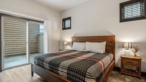 Een slaapkamer met een houten bed, een nachtkastje met een lamp, een klein tafeltje met een vaas en een schuifdeur naar een balkon.