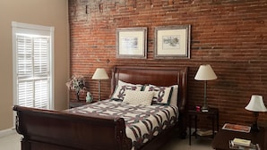 Un dormitorio con pared de ladrillo, una cama de madera, dos mesitas de noche con lámparas y un ventilador de techo.